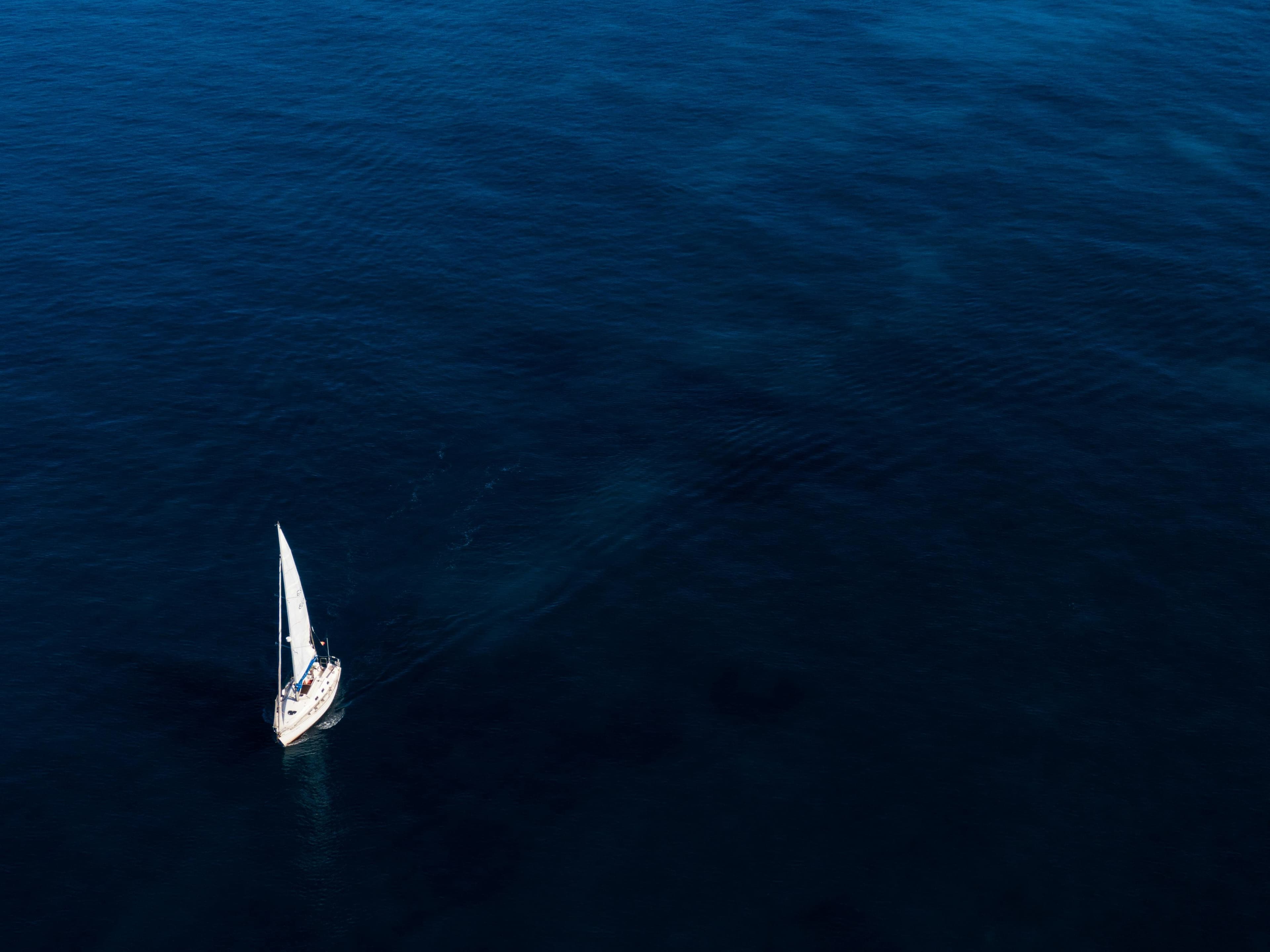 Veleiro solitário navegando em oceano profundo azul-navy, vista aérea